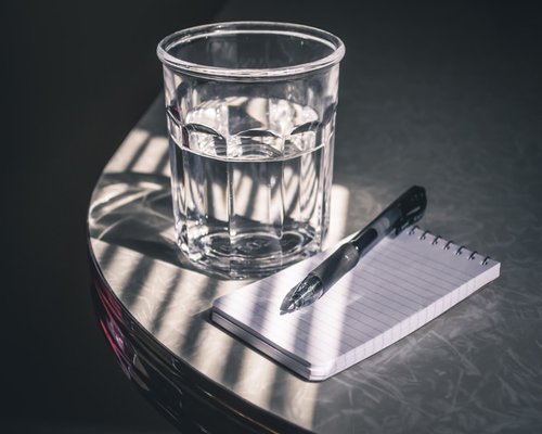 Close-up of clean notebook checklist items next to a clean glass of clear mineral water